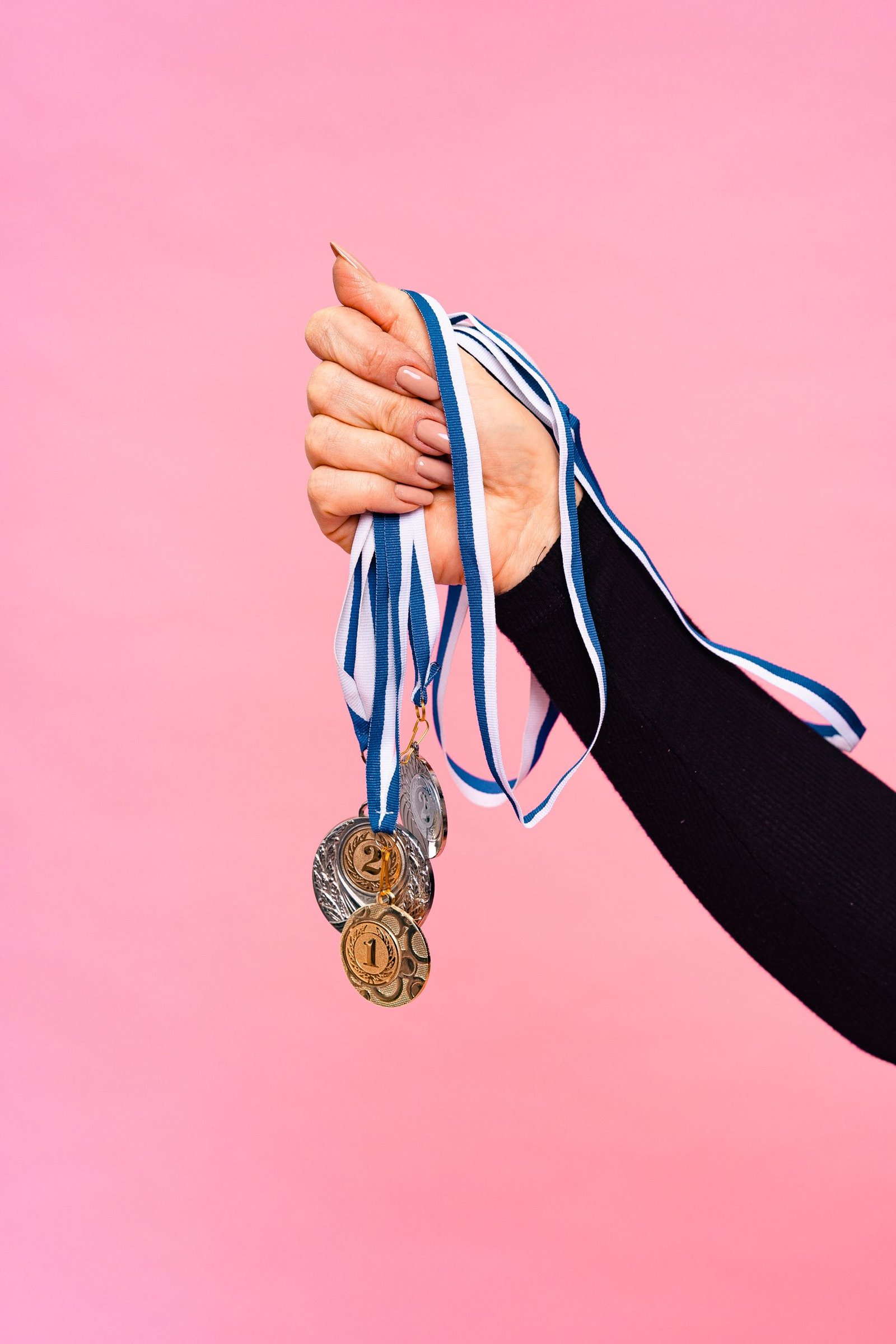 בית A hand holds multiple medals with blue ribbons against a pink background.