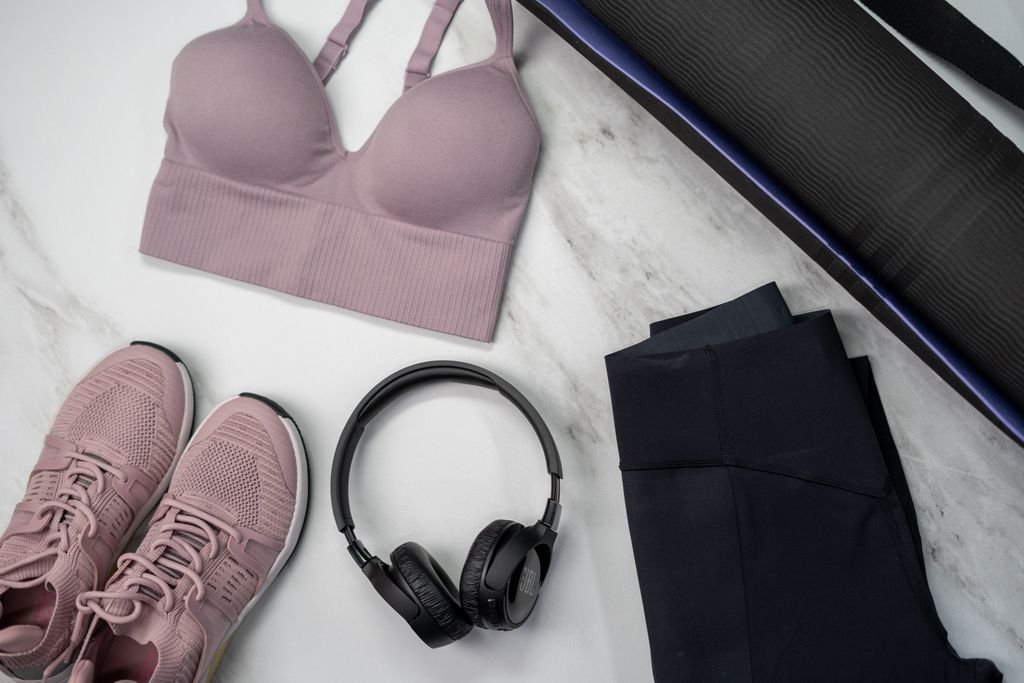 Flat lay of pink sportswear and accessories for a fitness routine on marble.