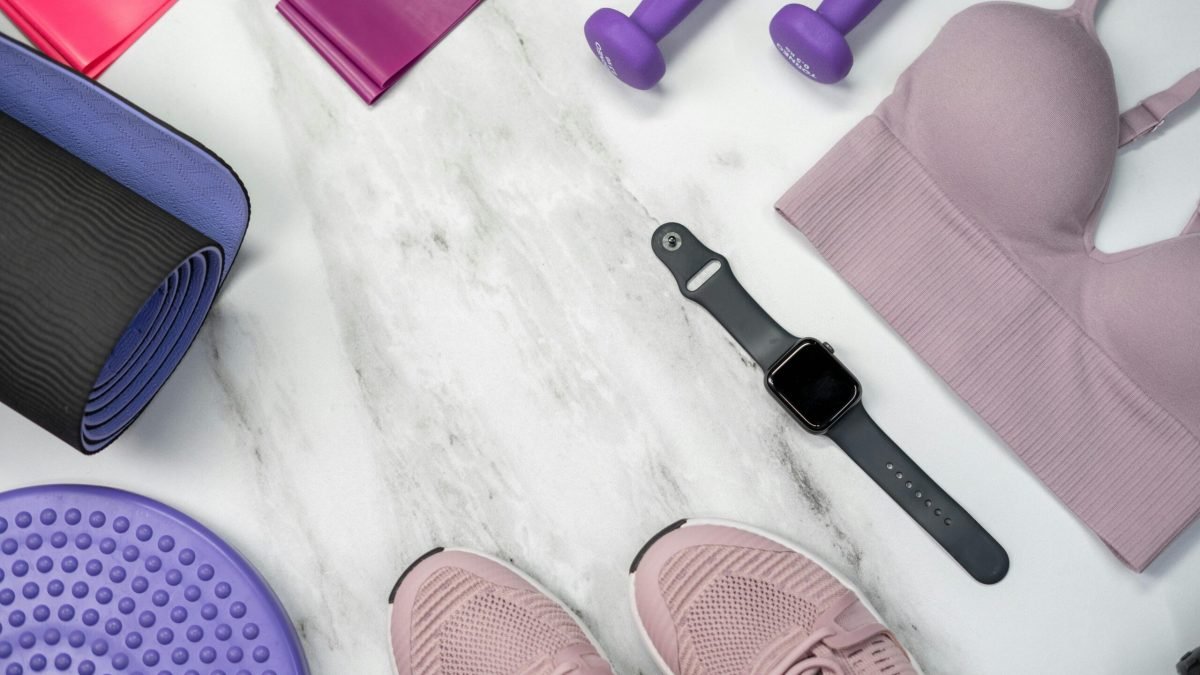 Flat lay of fitness gear including yoga mat, dumbbells, and smartwatch on a marble surface.