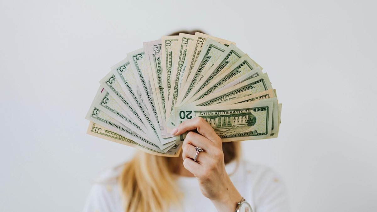 Close-up of a person holding a fan of US dollar bills on a neutral background.