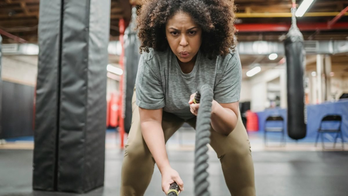 A determined woman performing a high-intensity battle rope exercise in a gym, showcasing strength and focus.