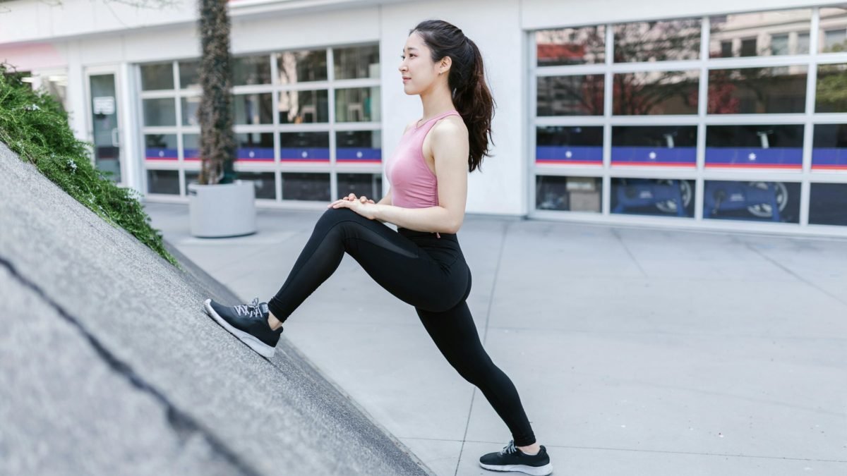Asian woman stretching outside against a city backdrop, emphasizing fitness and healthy lifestyle.