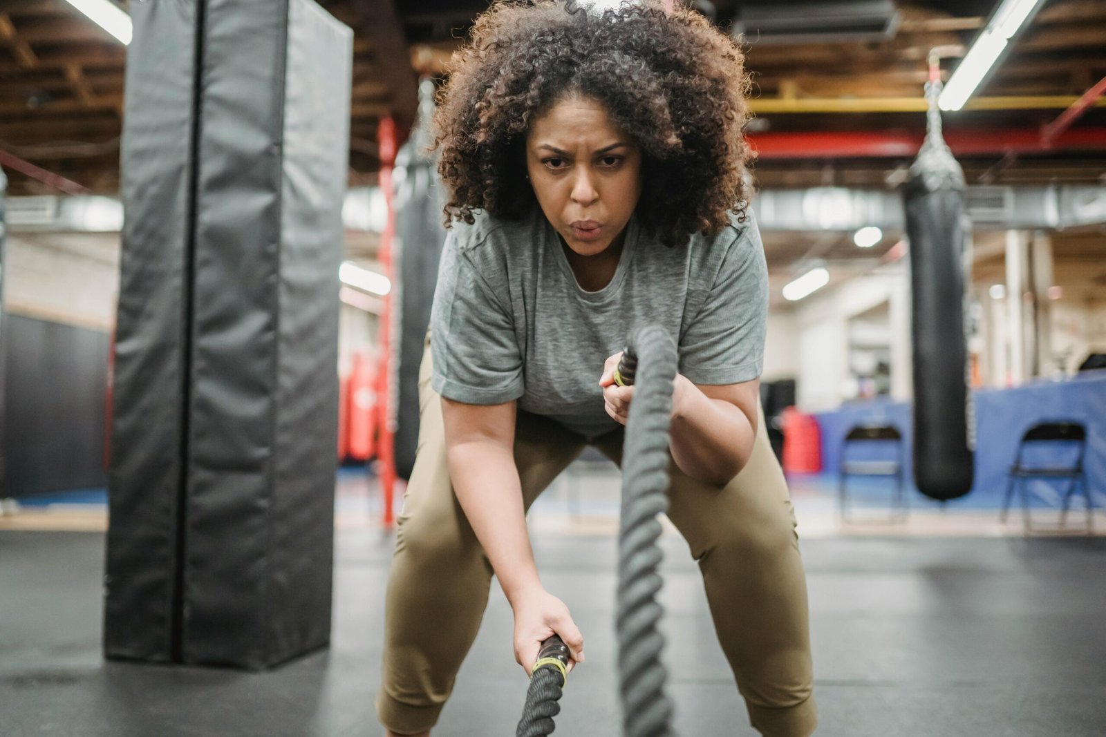 A determined woman performing a high-intensity battle rope exercise in a gym, showcasing strength and focus.