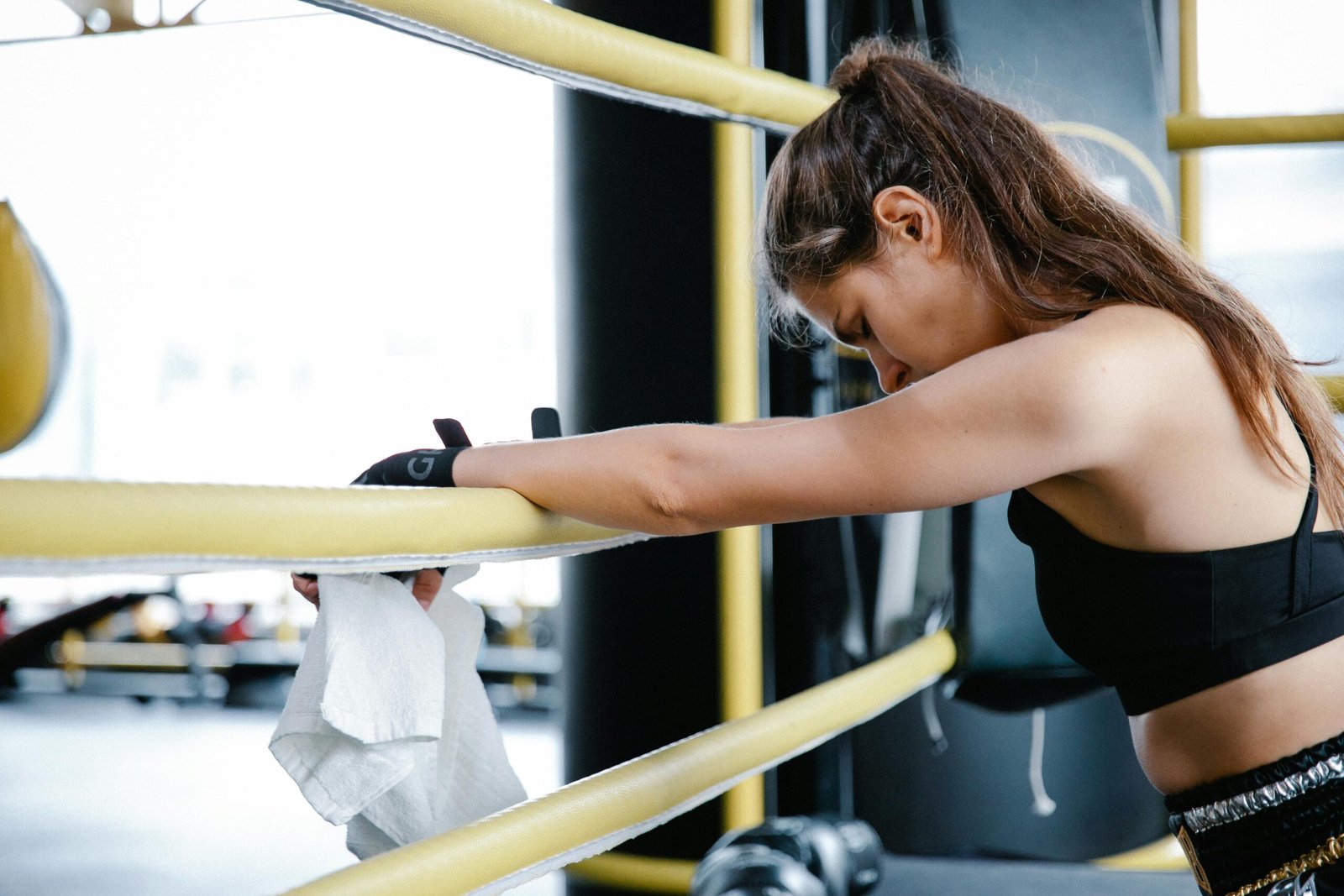 Exhausted woman in gym resting on boxing ring ropes wearing a crop top.